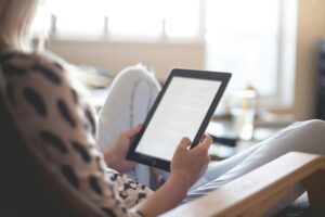A close-up image of a patient sitting in a cozy setting, engrossed in reading healthcare education resources on a digital tablet. The screen displays informative text and articles related to healthcare, emphasizing the patient's engagement with educational materials.