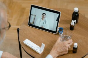 An image depicting an online doctor appointment. A doctor, dressed in professional attire, appears on the screen of a laptop. A patient, sitting comfortably at home, interacts with the doctor through the video call. The virtual consultation reflects modern healthcare accessibility.